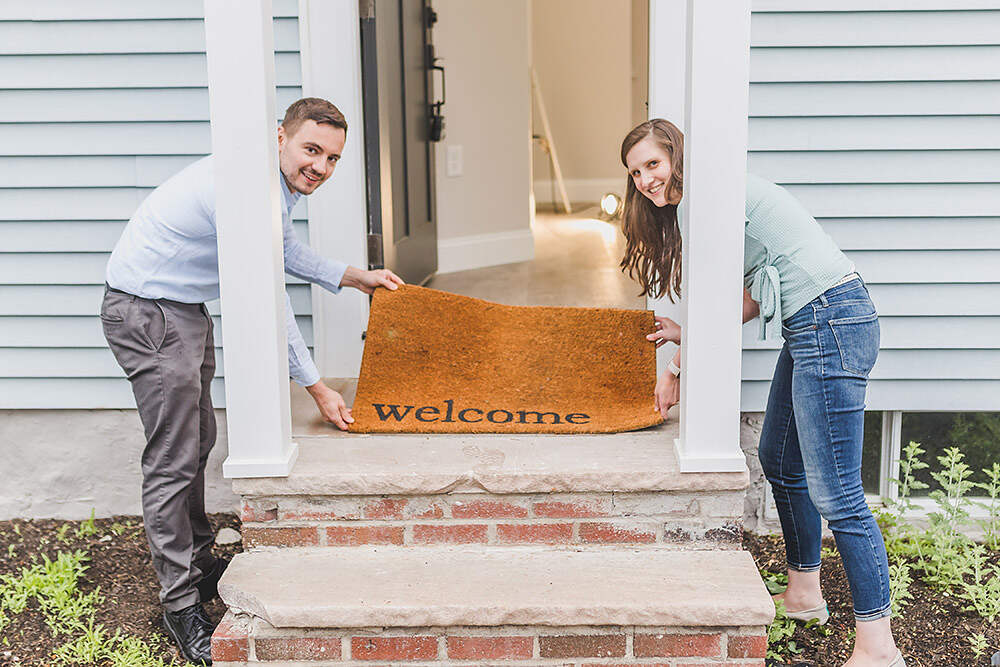 young couple holding up welcome mat